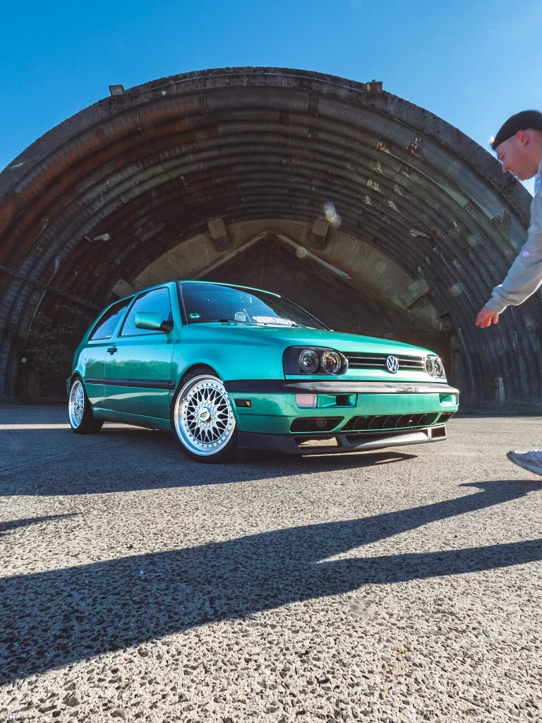 Ein teal VW Golf vor ein Hangar am Flughafengelände und sein Besitzer läuft davor. Foto bei Tobias Küpper - @pandalor
