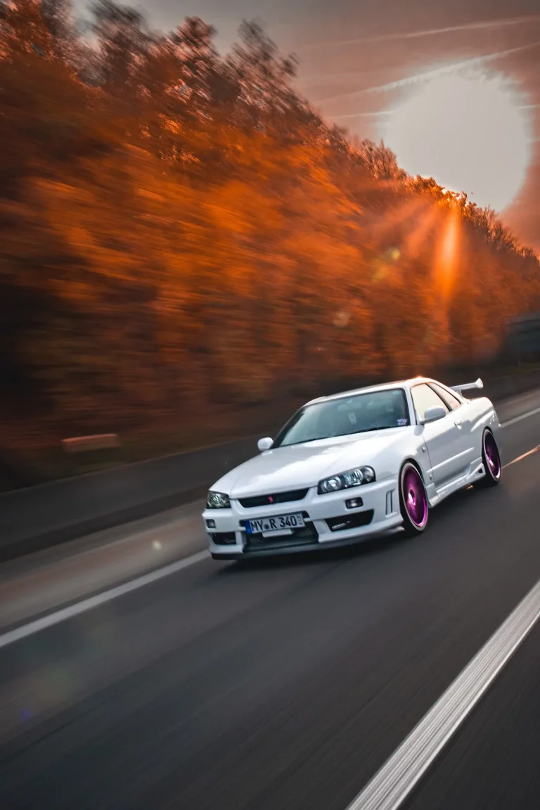 Ein weißer Nissan Skyline R34 GTT bei der Fahr während eines Sonnenuntergangs im Herbst. Bild bei Tobias Küpper - pandalor